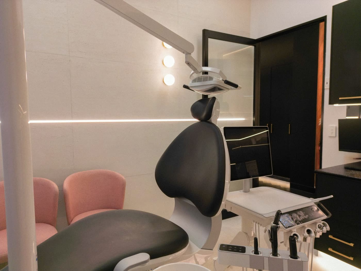 Treatment suite with a dental chair, soft pink seating and warm indirect lighting
